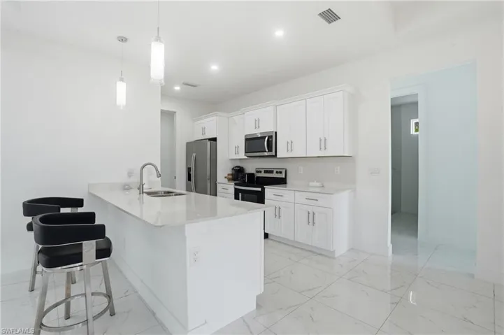 Kitchen with white cabinetry, a breakfast bar, a peninsula, light stone countertops, and stainless steel appliances