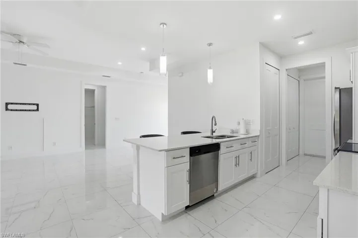 Kitchen with a peninsula, light stone countertops, a ceiling fan, light marble finish floors, and stainless steel appliances
