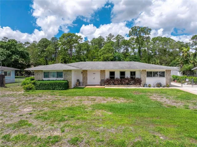 The property features a white exterior with stone accents, a gray roof, and a front yard with a lawn and shrubbery