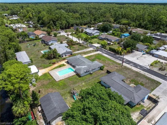 Aerial view showcasing the property with a rectangular pool, a well-maintained lawn, and mature trees