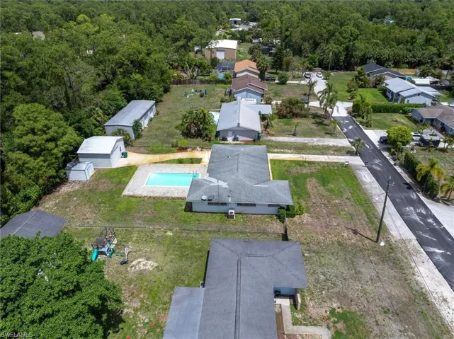 Aerial view of the property featuring an in-ground swimming pool, a drive, and surrounding green spaces with mature trees