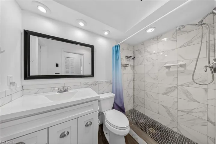 The bathroom features a modern vanity with a white countertop and sink, complemented by a large framed mirror