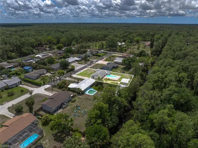 Aerial view showcasing the property with an outdoor swimming pool, a spacious yard, and surrounded by mature trees