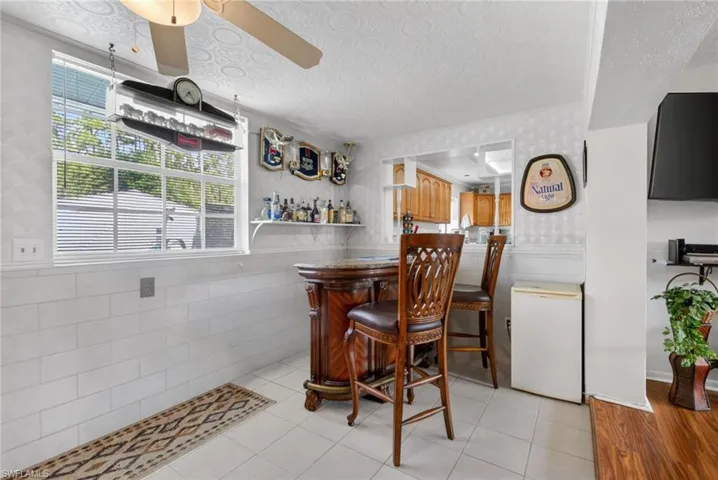 This space features a built-in bar with seating for two, white tiled flooring, and a ceiling fan