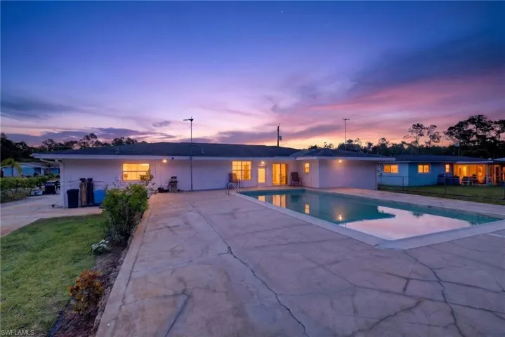 The property features an outdoor swimming pool, a spacious concrete patio, and a well-maintained lawn