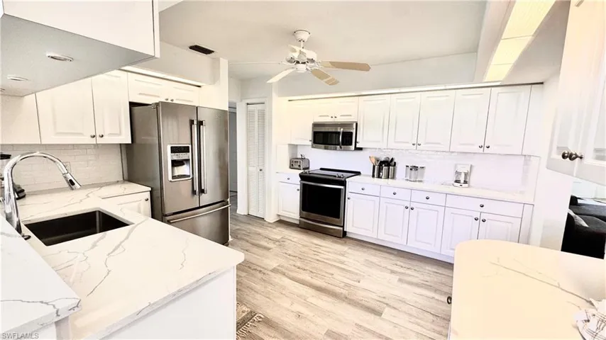 Kitchen with appliances with stainless steel finishes, ceiling fan, backsplash, and light wood-style floors