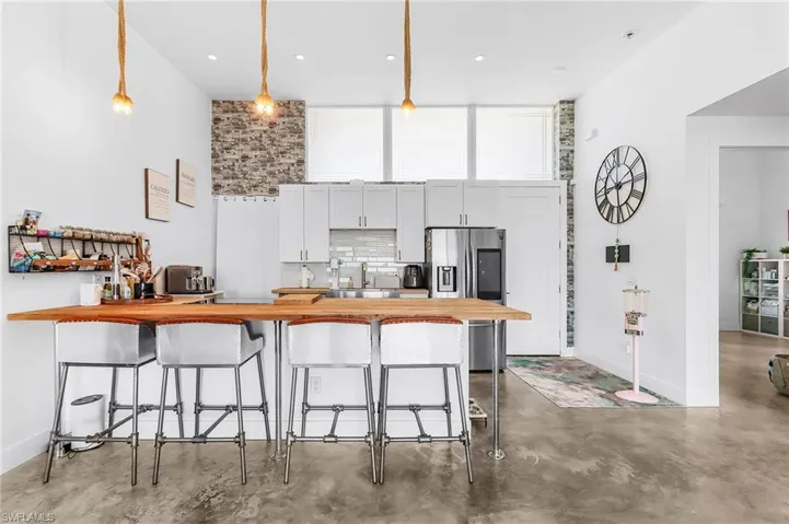 Kitchen featuring a peninsula, a breakfast bar area, stainless steel refrigerator with ice dispenser, finished concrete flooring, and white cabinets