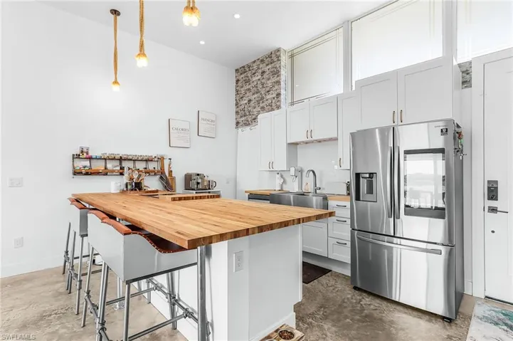 Kitchen with stainless steel fridge, unfinished concrete flooring, wooden counters, and pendant lighting