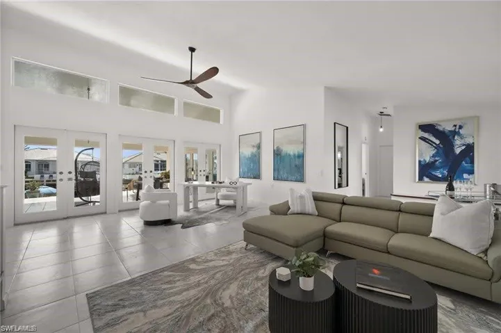 The living area features high ceilings, a ceiling fan, and large windows with French doors that provide an abundance of natural light and views of the surrounding properties and waterway