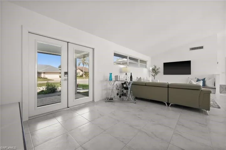 The dwelling features light-colored tile flooring throughout, white walls, and French doors that open to the exterior