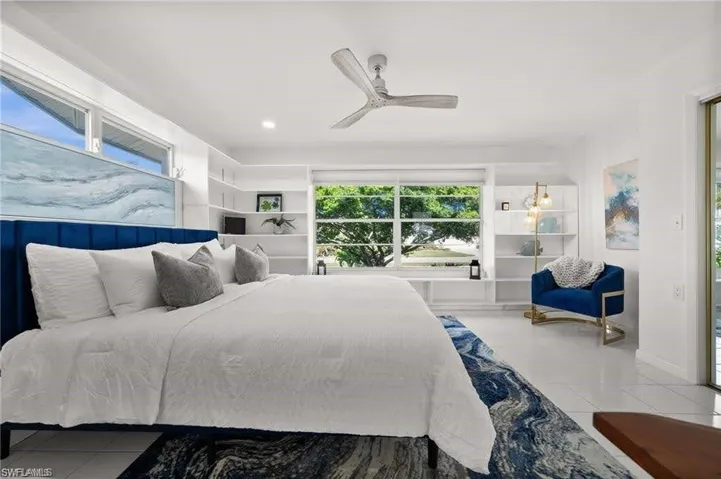 Bright bedroom featuring white walls, a large window with views of mature trees, and a ceiling fan
