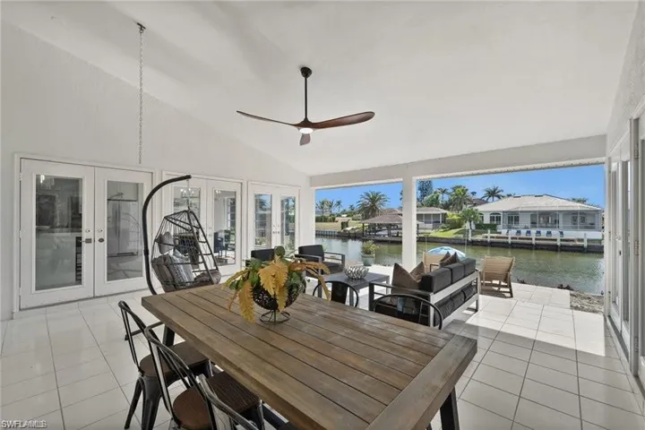 Expansive covered patio featuring white tile flooring, a sloped ceiling with a ceiling fan, and access to the outdoors through glass French doors