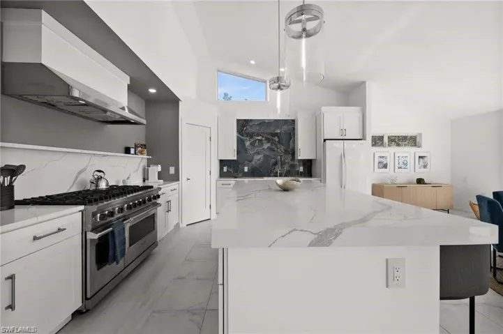 Remodeled kitchen featuring a large island with a substantial countertop, a professional-grade range with a stainless steel hood, and sleek white cabinetry