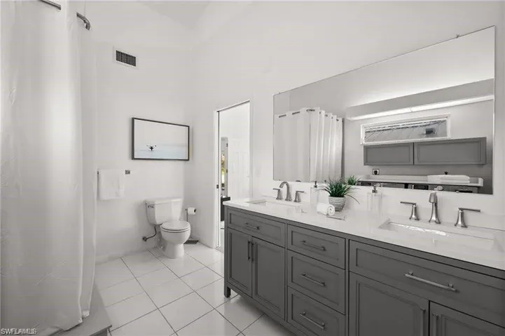The bathroom features a double vanity with grey cabinetry and white countertops, a large wall-mounted mirror, and white tile flooring