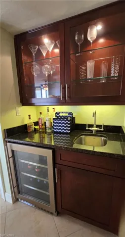 Bar with dark stone countertops, light tile patterned floors, beverage cooler, and sink