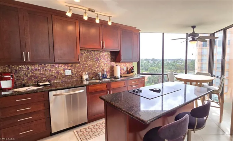 Kitchen with dark stone countertops, white electric cooktop, sink, and dishwasher