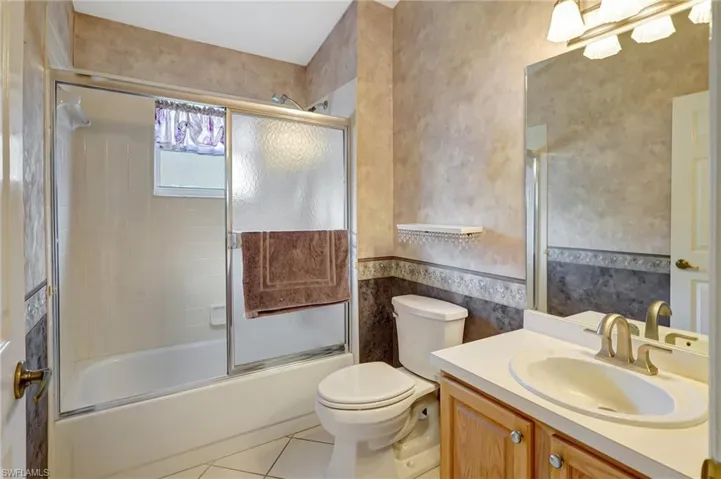 Full bath featuring tile patterned floors, vanity, toilet, and enclosed tub / shower combo
