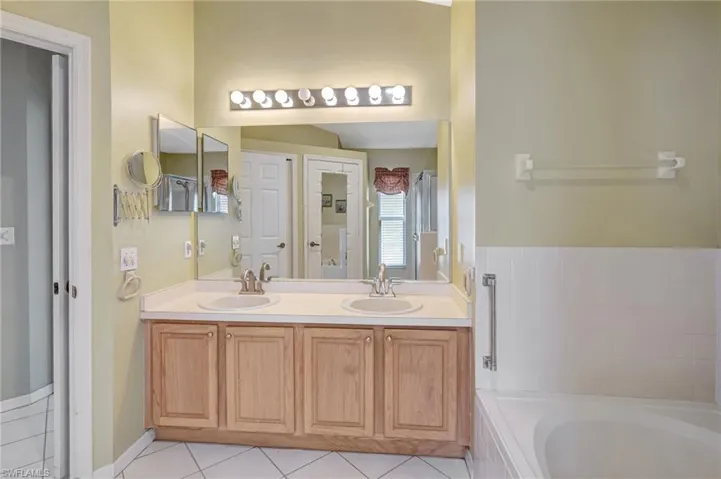 Full bathroom featuring tile patterned floors, a sink, double vanity, and a bath