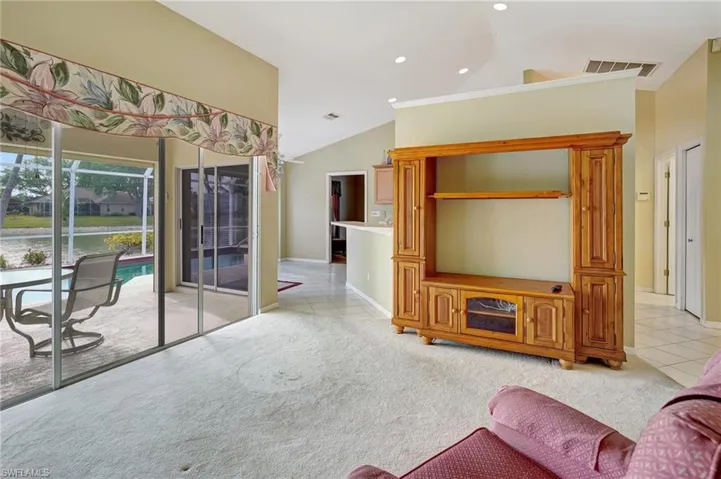 Living room featuring visible vents, vaulted ceiling, light tile patterned floors, and light colored carpet