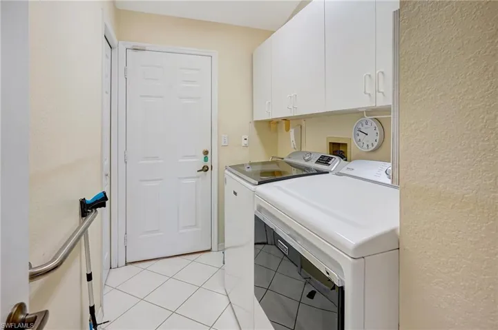 Clothes washing area with independent washer and dryer, light tile patterned flooring, and cabinet space