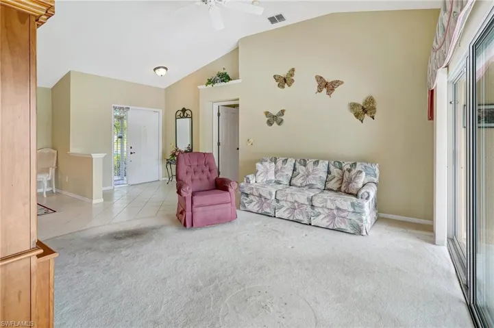 Living area with tile patterned flooring, high vaulted ceiling, carpet floors, ceiling fan, and visible vents