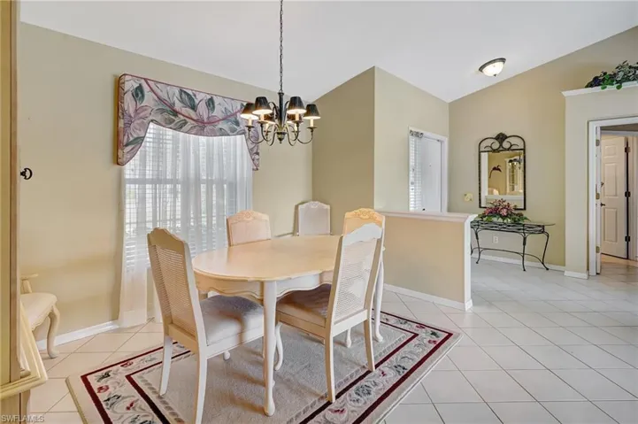 Dining room featuring light tile patterned flooring, baseboards, vaulted ceiling, and a chandelier