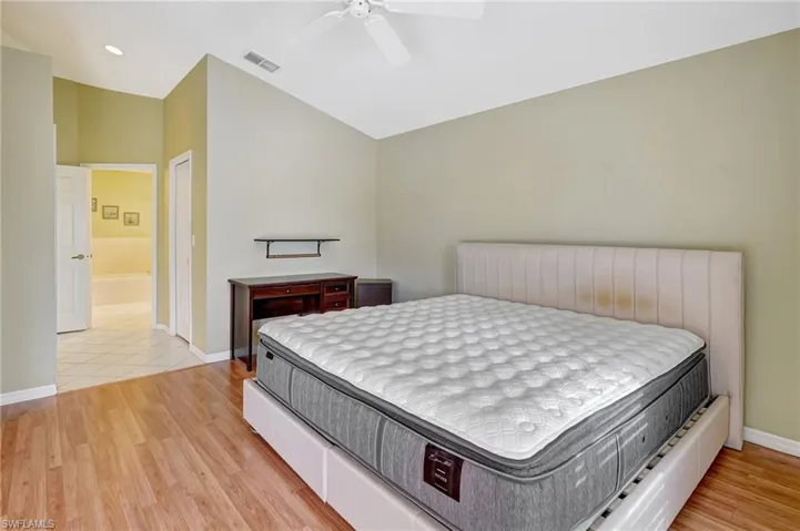 Bedroom with vaulted ceiling, a ceiling fan, light wood-type flooring, baseboards, and visible vents