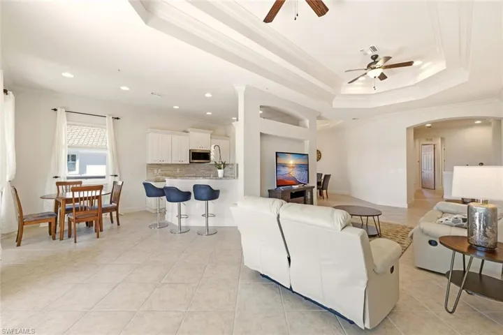 Living area with crown molding, ceiling fan, arched walkways, light tile patterned floors, and a tray ceiling