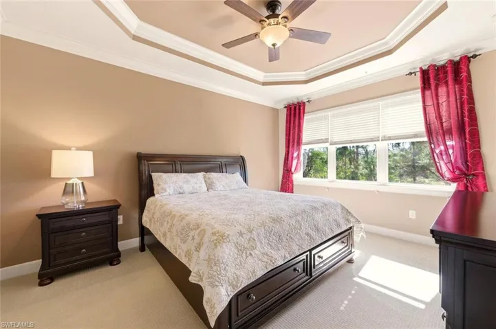Bedroom with a tray ceiling, crown molding, light carpet, and ceiling fan