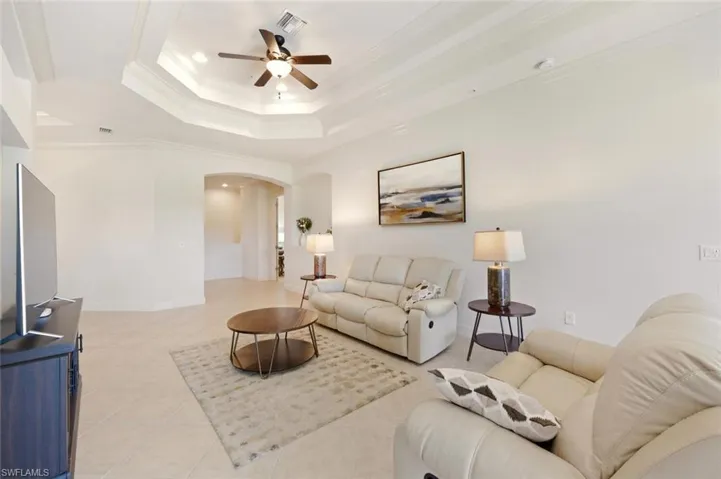 Living room with arched walkways, a tray ceiling, crown molding, ceiling fan, and light tile patterned floors