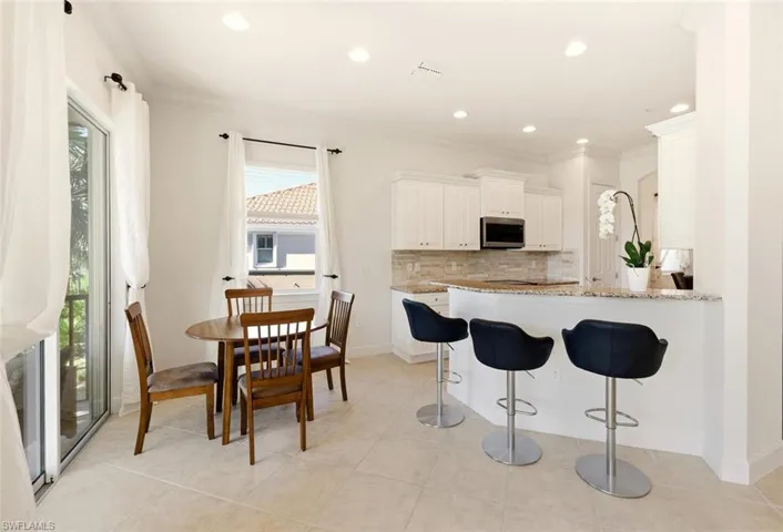 Kitchen featuring a breakfast bar area, light stone counters, backsplash, a peninsula, and white cabinets