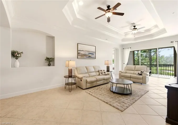 Living area featuring ceiling fan, ornamental molding, light tile patterned floors, and a raised ceiling