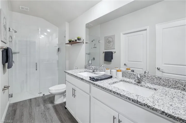 Bathroom featuring a stall shower, double vanity, and dark wood-style flooring
