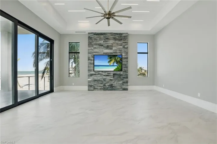 Unfurnished living room featuring a tray ceiling, light marble finish flooring, and a ceiling fan Virtually Enhanced