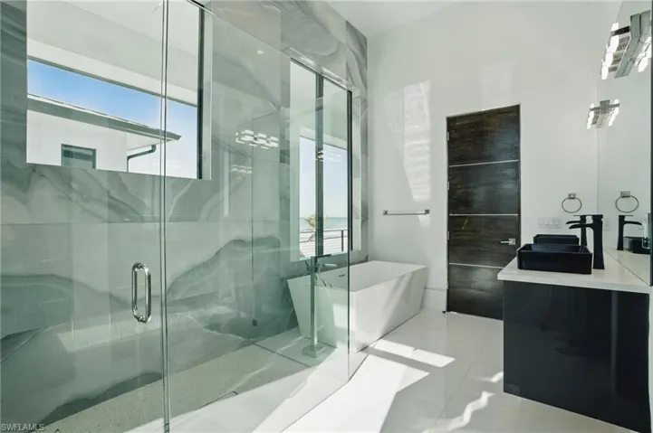 Full bathroom featuring vanity, a freestanding bath, plenty of natural light, and a marble finish shower Virtually Enhanced