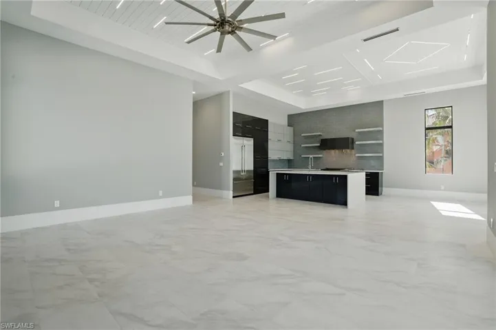 Unfurnished living room featuring light marble finish floors, a wooden tray ceiling, and ceiling fanVirtually Enhanced