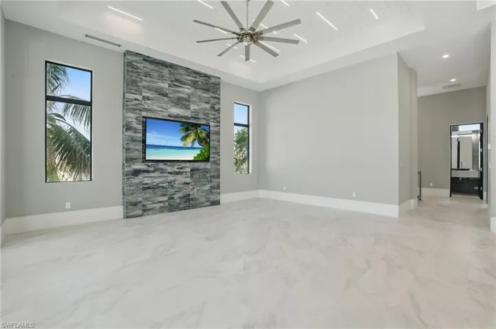 Unfurnished living room with a wooden tray ceiling, a ceiling fan, and light marble finish floorsVirtually Enhanced