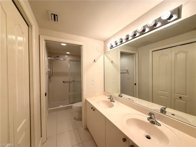 Full bath with a stall shower, double vanity, light tile patterned floors, and a closet