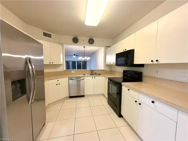 Kitchen with black appliances, white cabinetry, a chandelier, and light countertops