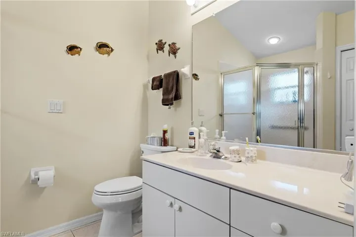 Bathroom with vanity, lofted ceiling, tile patterned floors, toilet, and walk in shower