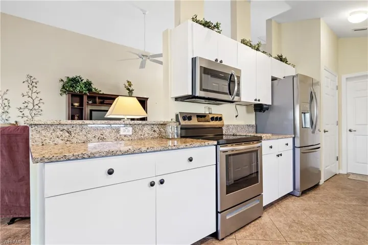 Kitchen featuring white cabinets, ceiling fan, light stone countertops, light tile patterned floors, and stainless steel appliances