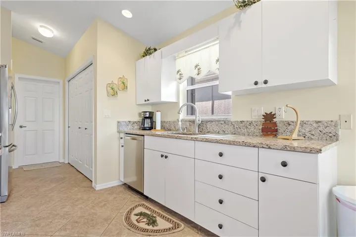 Kitchen featuring lofted ceiling, sink, appliances with stainless steel finishes, light stone counters, and white cabinetry