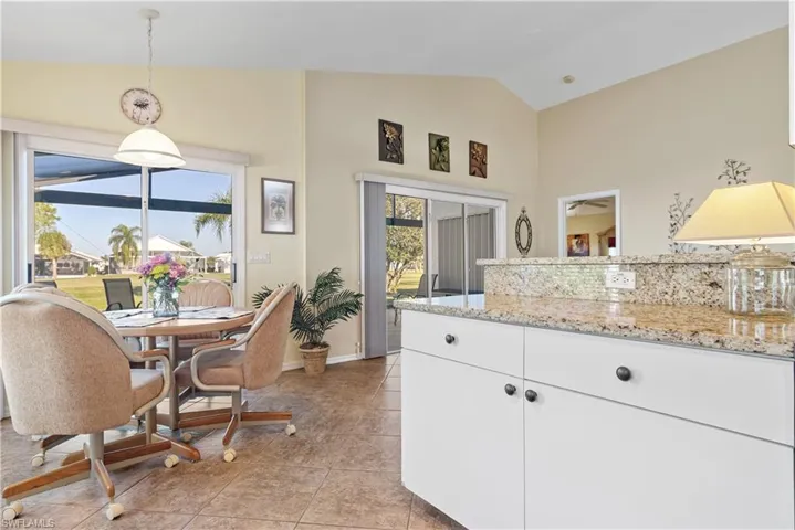 Kitchen with light stone counters, white cabinets, hanging light fixtures, and lofted ceiling