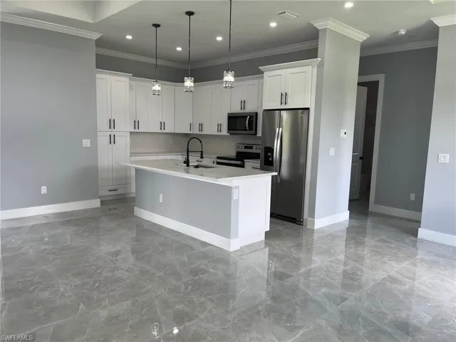 Kitchen featuring sink, appliances with stainless steel finishes, crown molding, and a center island with sink