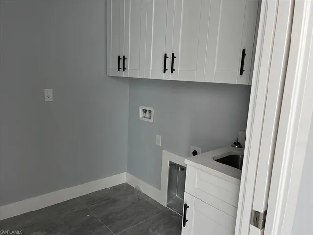 Laundry room with cabinets, hookup for an electric dryer, hookup for a washing machine, sink, and dark tile floors