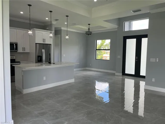 Kitchen featuring tile patterned flooring, white cabinets, a kitchen island with sink, stainless steel appliances, and hanging light fixtures