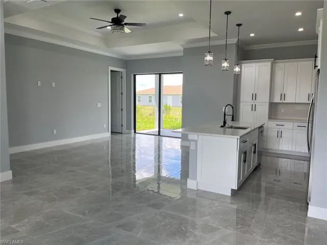 Kitchen featuring ceiling fan, crown molding, an island with sink, sink, and a raised ceiling