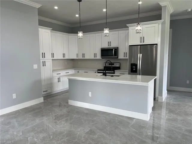Kitchen with stainless steel appliances, sink, pendant lighting, an island with sink, and white cabinetry
