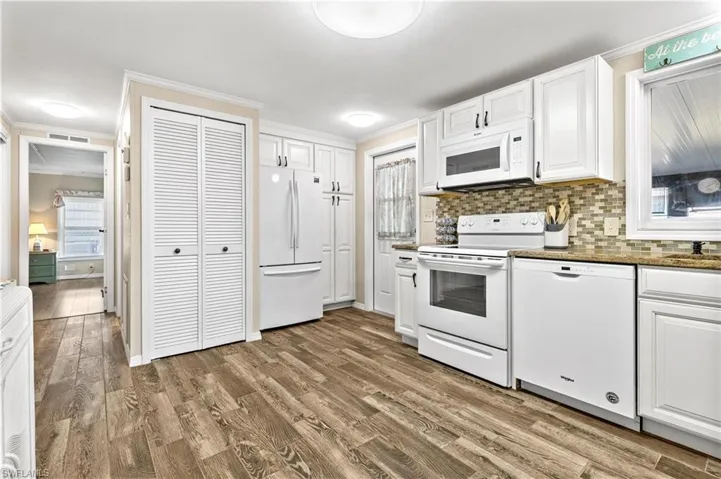 Kitchen with white appliances, white cabinets, backsplash, and wood-type flooring