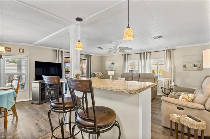 Kitchen featuring decorative light fixtures, crown molding, a breakfast bar area, light stone countertops, and wood-type flooring